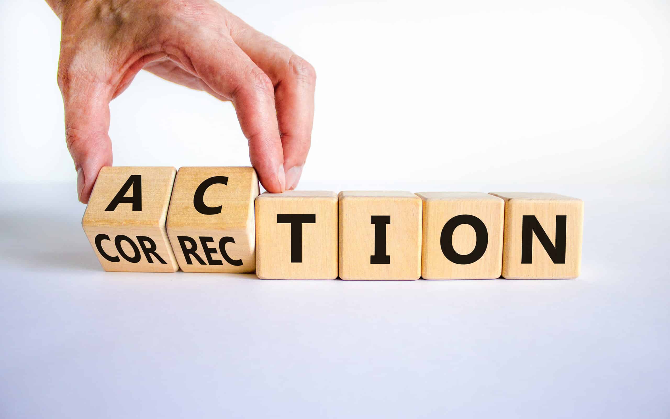 Wooden blocks that show the word correction turning to action. A hand is moving the blocks