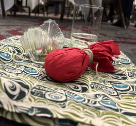 Red tobacco tie with a glass of water and bowl on a West Coast Indigenous cloth on the floor