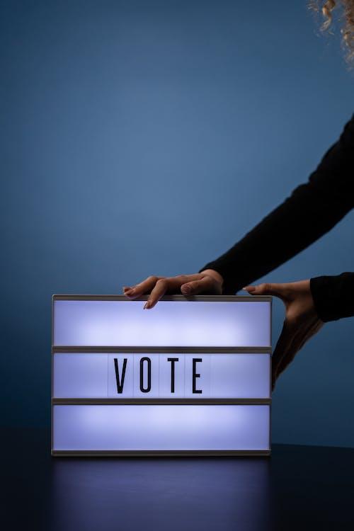 Two hands resting on a lighted box with the words "vote" on it.