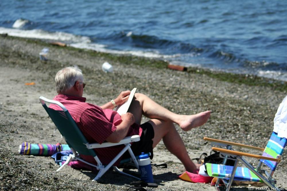 Man sitting on chair on beach near water, with books